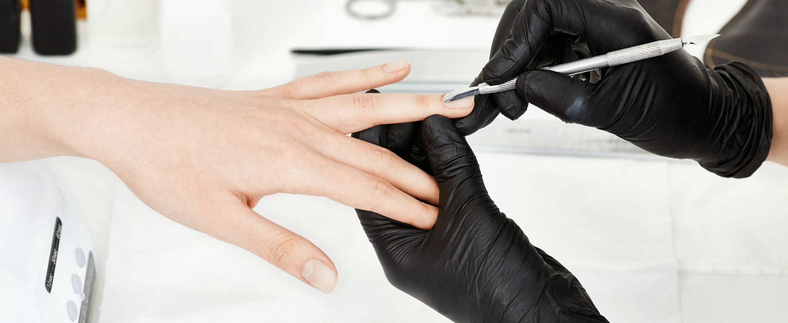 Manicrurist in gloves pushing cuticle on woman's ring finger.